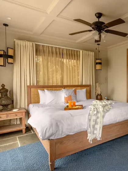 A wider view of the bedroom, showcasing the coffered ceiling and the use of natural materials like wood and stone. The color palette is intentionally muted to keep the focus on the incredible views outside.