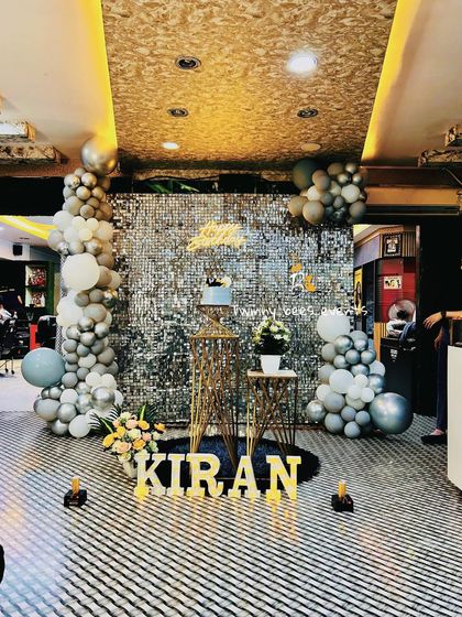 A glamorous party setup in a salon. We used a silver shimmer wall, a grey and white balloon garland, and marquee letters to transform the space for Kiran's birthday.