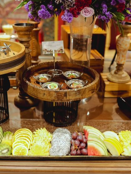 A grand buffet table featuring a long platter of artistically sliced exotic fruits alongside other Indian appetizers. The combination of colors and textures is visually stunning.
