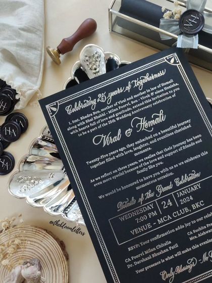 The full view of the elegant black and silver 25th-anniversary invitation, laid out with the custom wax seals and stamper.