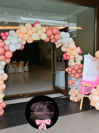 The entrance to the baptism party, with a beautiful balloon arch in a soft, multi-toned pink and peach palette. A personalized welcome sign greets the guests.