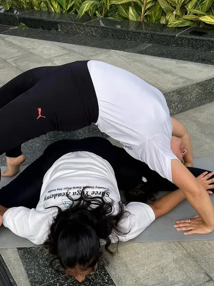 This partner pose combines a deep forward fold (Upavistha Konasana) with a full backbend (Chakrasana). It's an advanced expression of flexibility and mutual support.