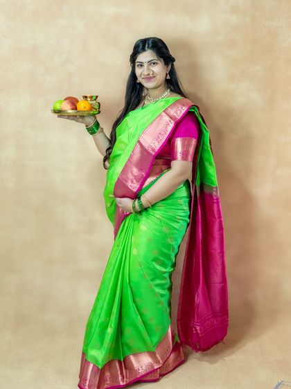 A graceful studio portrait of a mom-to-be in a traditional green saree, holding a plate of offerings.