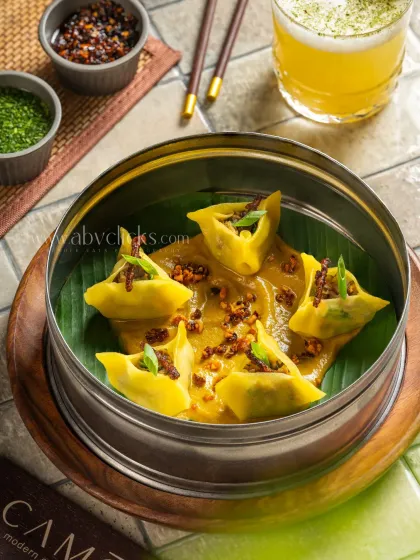 Yellow dim sum in a savory sauce, presented in a steamer for Camo, Noida.