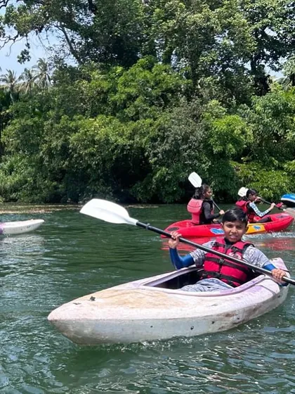 A young boy enjoys a solo paddle in his kayak on the calm waters of the Kali River, surrounded by the beautiful forests of Dandeli.