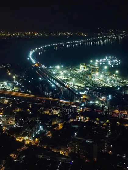 A wide drone shot captures the scale of the Trans Harbour Link at night, its lights creating a bright curve against the dark sea.