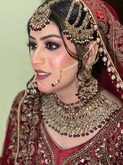A stunning side profile of this bride. Her elaborate jewellery, including the multi-layered headpiece and nath, is the star of the show, complemented by sharp, winged eyeliner and a matte lip.