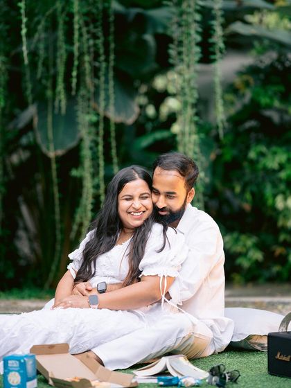 An intimate picnic-style pre-wedding shoot. The couple relaxes on the lawn, surrounded by the giant leaves of our tropical plants, creating a cozy and romantic scene.