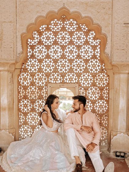 An intimate moment framed by a stunningly intricate marble lattice (jaali) in a Jaipur palace. The soft light filtering through creates a dreamy and romantic atmosphere for this pre-wedding portrait.