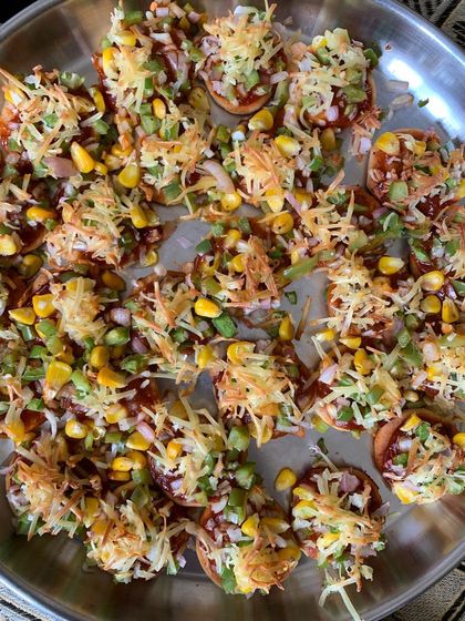 A tray of mini pizzas topped with cheese, corn, and veggies.
