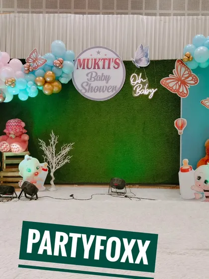 A butterfly-themed baby shower for Mukti, with a green backdrop, pastel balloons, and cute teddy bear props.