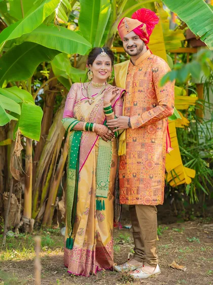 A classic portrait of a Maharashtrian couple amidst banana plants, a traditional element in many Indian weddings, highlighting their beautiful wedding attire.