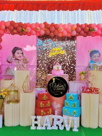 A first birthday celebration with a pink and gold theme. The setup includes a shimmer wall, custom photo banners, and a large marquee number '1'.