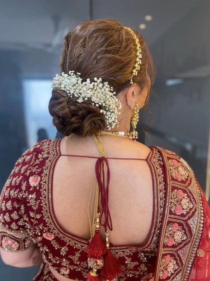 This beautiful bridal messy bun is adorned with a classic arch of white baby's breath, a timeless and elegant choice for any bride.