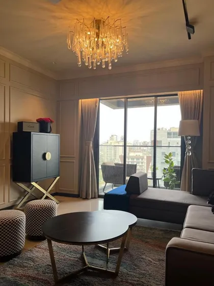 This living room combines classic comfort with modern glamour, featuring a plush chaise lounge, a stunning glass chandelier, and a balcony that extends the living space. The bespoke cabinet adds a touch of art deco elegance.
