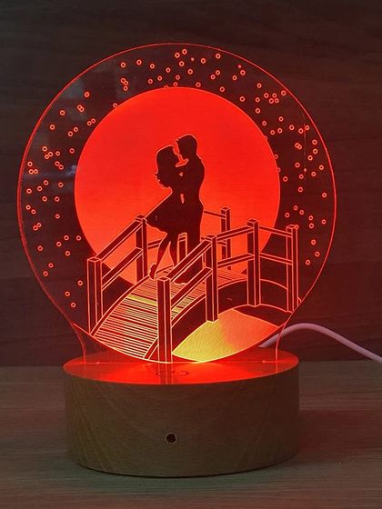 This silhouette lamp shows a romantic scene of a couple on a bridge against a full moon. The design is etched into acrylic and lit from the base, creating a beautiful 3D effect.