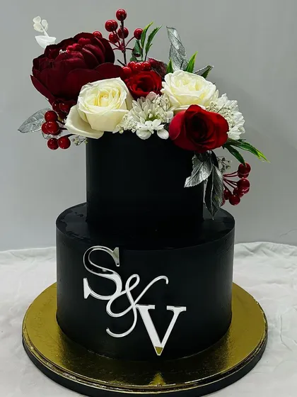 Bold and sophisticated. This two-tiered black cake is decorated with a stunning arrangement of red and white flowers and a custom silver monogram, perfect for a modern wedding or engagement.