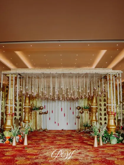An elegant indoor mandap with golden pillars and strings of white jasmine. The design brings traditional grandeur into a classic ballroom setting for a timeless wedding ceremony.