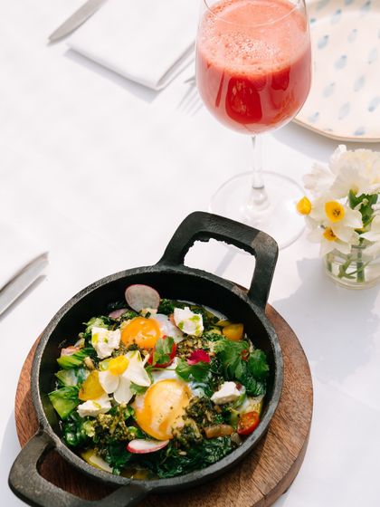 Our Green Shakshuka, a vibrant dish of baked eggs in a skillet with fresh greens and feta, paired with a refreshing glass of watermelon juice.