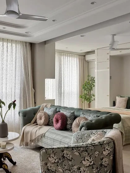 An open-concept space where the living area flows into a bedroom zone. The floral sofa and layered pillows create a soft, inviting foreground to the tranquil sleeping area beyond.
