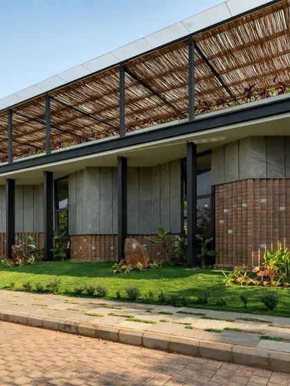 The exterior of 'The Earth' combines dry-clad granite on the upper level with a lower band of CSEB blocks, all sheltered under a light, bamboo-thatched pergola.