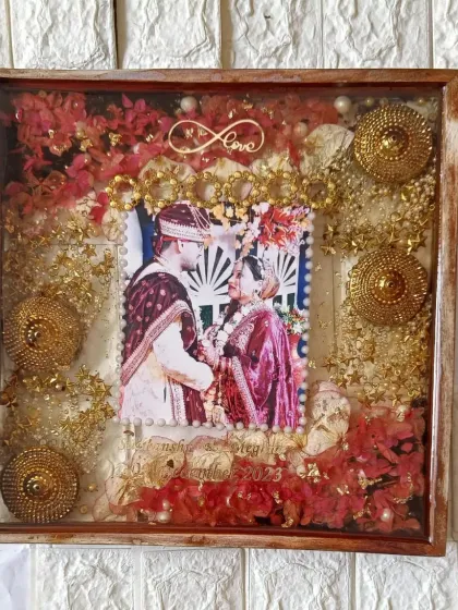 This square frame is full of festive details, including preserved red flowers, golden kaleere accents, and an infinity symbol. It's a vibrant celebration of the couple's union.