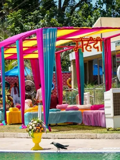 A colorful Mehendi seating area by the pool. The vibrant drapes and comfortable divans create a perfect spot for guests to get their henna done while enjoying the party.