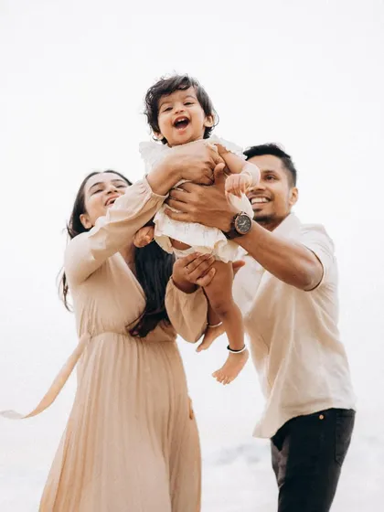 Pure happiness as parents lift their laughing baby into the air during a bright day at the beach. This photo is all about capturing the energy and delight of candid child photography.