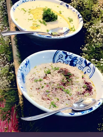 A display of creamy dips, including hummus topped with olive oil and a garnished baba ghanoush, nestled in a bed of fresh baby's breath.
