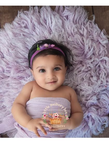 At 10 months old, babies are so expressive. This little one is lying on a soft purple blanket, looking right at the camera with her big, beautiful eyes.