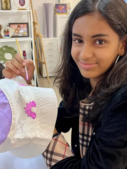 A participant carefully paints purple flowers on her hat, enjoying the creative process at a birthday party.