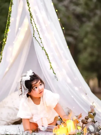 Looking up in wonder. The fairy lights in the tent create a magical sparkle in her eyes.