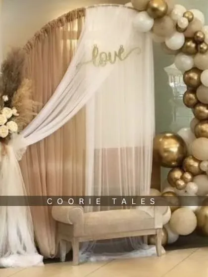 A dreamy boho setup for an intimate anniversary celebration. This design features a golden arch draped with sheer fabric, a neutral balloon garland, and dried florals, creating a warm and romantic atmosphere.