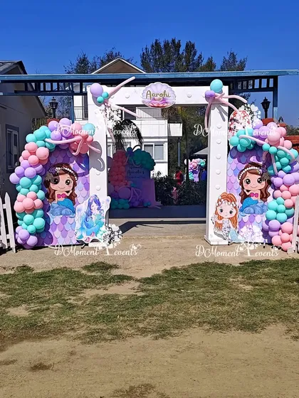 An outdoor entrance for a mermaid-themed party. The white archway is decorated with pastel balloon garlands and cute mermaid character cutouts, perfect for a fun-filled celebration at a farmhouse.