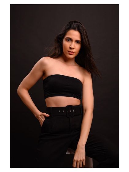 A simple and chic studio portrait. The model wears a black tube top and belted trousers, creating a minimalist look that is both modern and timeless.