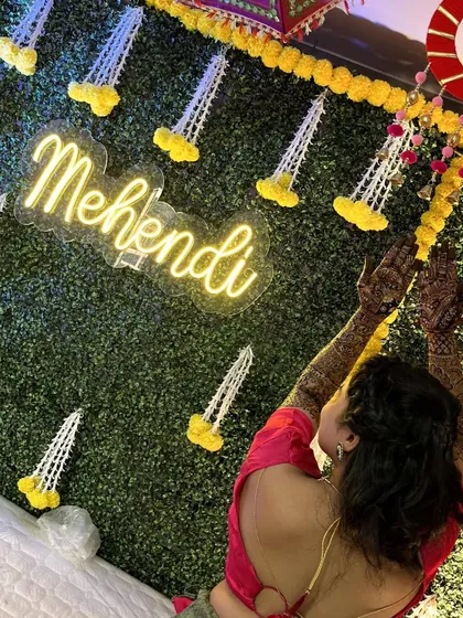 The 'Mehendi' neon sign and hanging floral tassels create a perfect frame for the bride's photos.