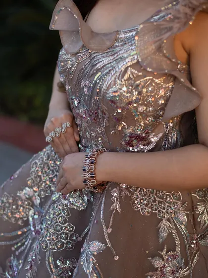 A close-up on the exquisite details of our rose gold organza gown. The combination of silver and multi-color embroidery, sparkling crystals, and soft ruffles creates a rich and luxurious texture.