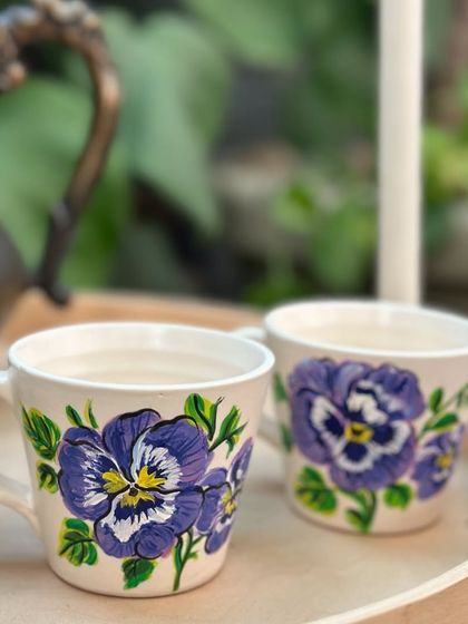 A pair of ceramic cups hand-painted with delicate purple pansy flowers.