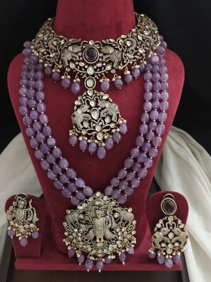 This complete bridal set in lavender includes a choker, a short necklace, and a long necklace, all with matching earrings. The intricate designs feature deities and peacocks.