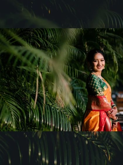 A beautiful bridal portrait of the bride smiling, framed by lush green foliage that makes her colorful saree pop.