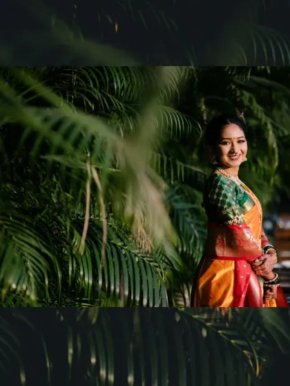A beautiful bridal portrait of the bride smiling, framed by lush green foliage that makes her colorful saree pop.