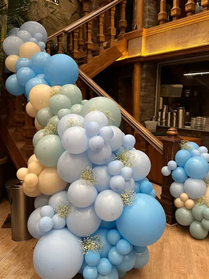 A stunning balloon garland in shades of blue, cream, and mint cascaded down the staircase, creating a grand and festive entrance for the baby celebration.