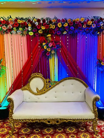 A straight-on shot of the reception stage with full lighting. The combination of colorful drapes, a dense flower border, and a classic white sofa creates a perfect backdrop for wedding photos.