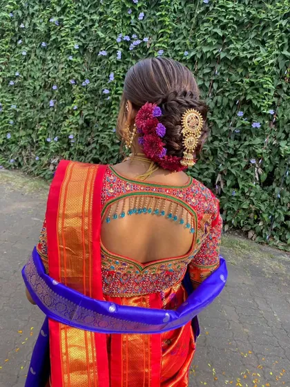 A back view of the bride's stunning hairstyle. The braided bun is adorned with purple flowers and a beautiful gold accessory, matching her blouse perfectly.