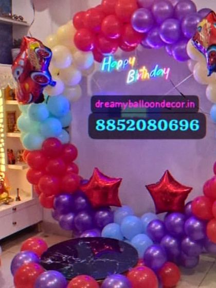 A high-energy birthday party with a Disney 'Cars' theme. This decoration features a colorful balloon ring with Lightning McQueen cutouts, a neon 'Happy Birthday' sign, and a balloon pillar with the age number.
