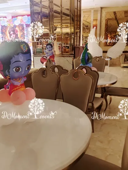 Table decor for the Krishna-themed party, featuring small cutouts of Little Krishna and peacock balloons, ensuring the theme is carried throughout the entire venue.