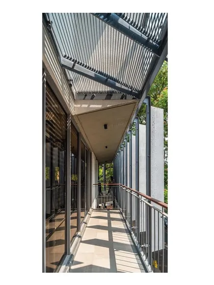 A view from one of the staggered balconies, looking along the facade. The interplay of light and shadow created by the overhead screen and vertical fins creates a dynamic and comfortable semi-outdoor space, extending the usable area of the office.