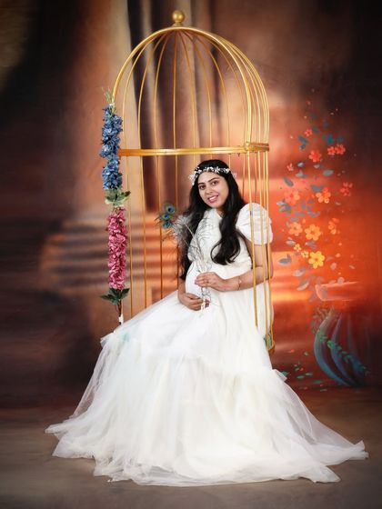 A creative studio maternity shoot using a golden birdcage prop. Our white ruffled gown adds to the whimsical and fairytale-like theme of the photograph.
