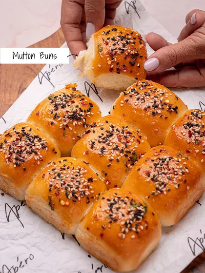 A hand reaching for one of our savory Mutton Buns. These soft buns are filled with spiced mutton and topped with sesame seeds, making for a delicious and satisfying snack.