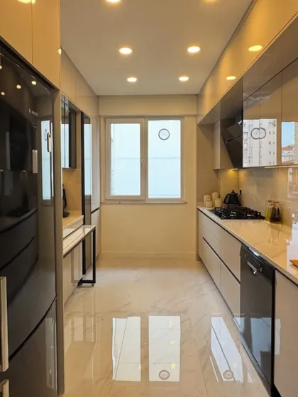 Another view of the Neeti Bagh galley kitchen, showing the efficient layout from the opposite end. The glossy surfaces and light colors help make the space feel larger and brighter.